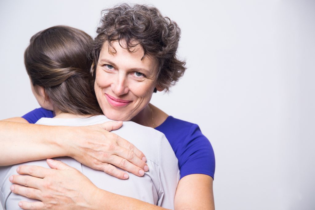 Studio portrait of happy senior woman embracing young adult daughter, looking at camera and smiling